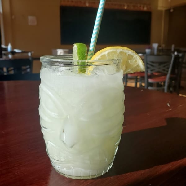A refreshing Bombay Social cocktail in a tiki glass, garnished with lime and lemon slices, on a wooden table.