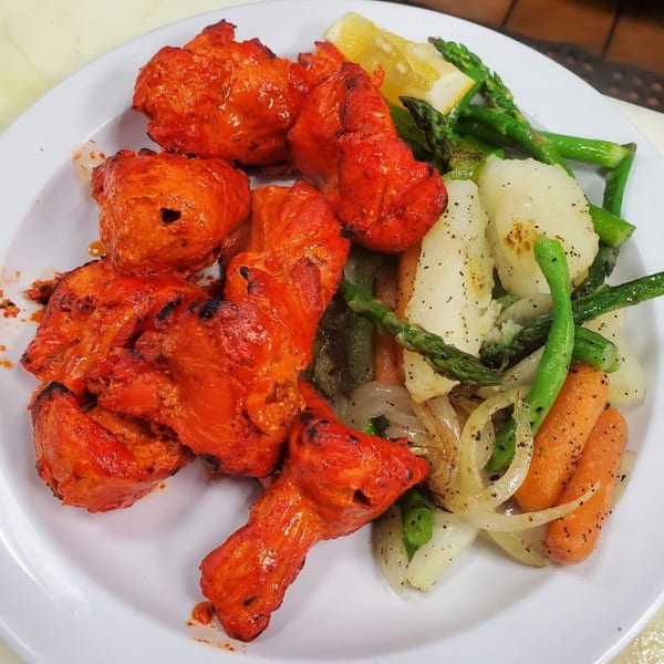 Bombay Social's vibrant red chicken tikka with roasted vegetables and a lemon wedge on a white plate.