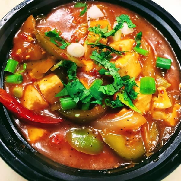 Close-up of Bombay Social's chili paneer with peppers, onions, and cilantro in a rich red sauce.