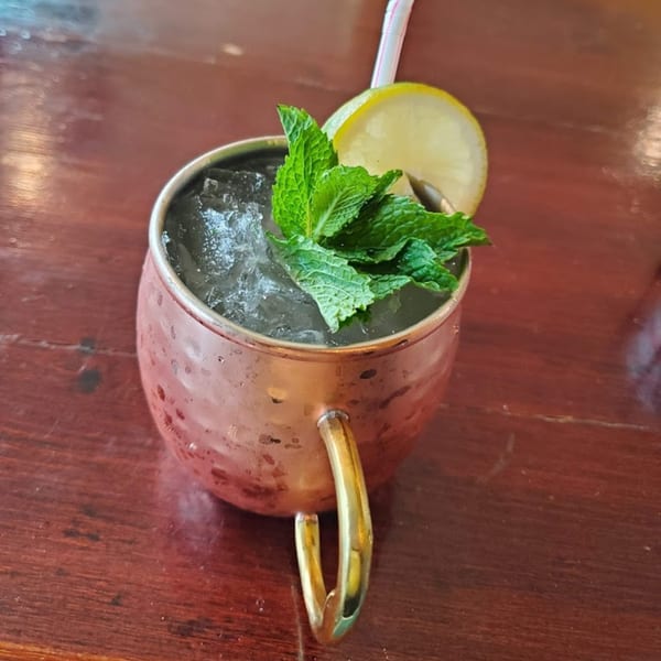 A Bombay Social cocktail in a copper mug with ice, mint, and a lemon slice.