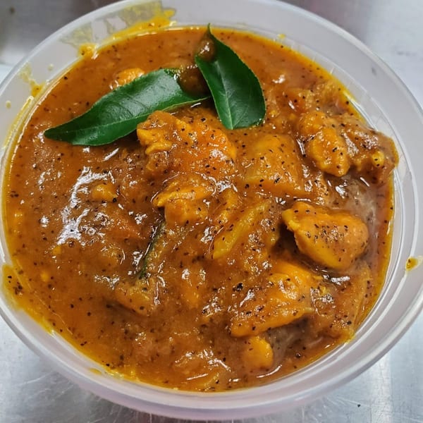 Close-up of Bombay Social's Indian chicken curry, garnished with fresh green leaves in a clear bowl.