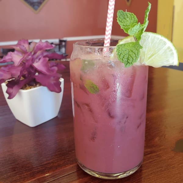 A vibrant pink drink with a striped straw, lime, and mint garnish, next to a small plant.