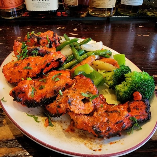Platter of Bombay Social's chicken tikka with grilled green beans, onions, carrots, and broccoli.