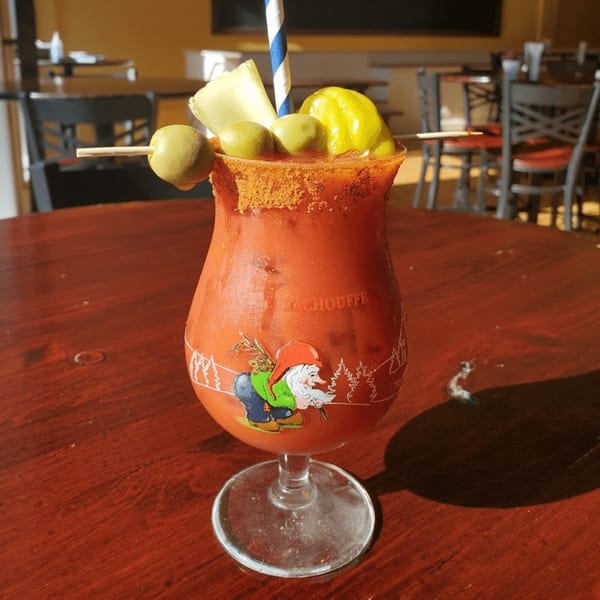 A Bloody Mary cocktail in a gnome-decorated glass, garnished with olives, cheese, and a pepper.