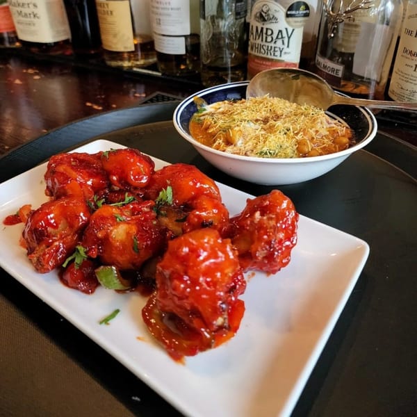Bombay Social's chili chicken and a bowl of Indian chaat with crispy noodles, against a bar background.