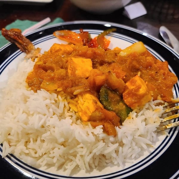 Indian paneer curry with bell peppers and onions, served over white rice on a striped plate.