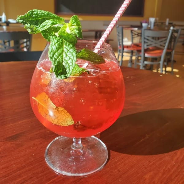 A vibrant red cocktail with mint garnish and a striped straw sits on a wooden table.